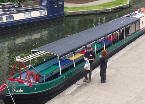 Green-painted narrowboat seen from above at an angle. moored on a wharf