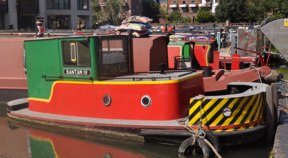 Red and green short boat with buildings and boats behind