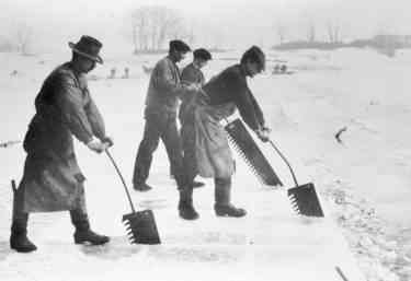 Han saws on long handles being used to cut ice in a lake
