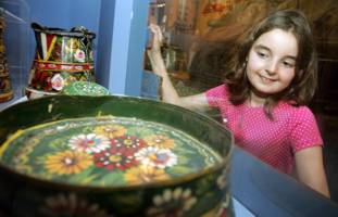 A girl looks through the glass at a display of items painted in the traditional style of "roses and Castles"
